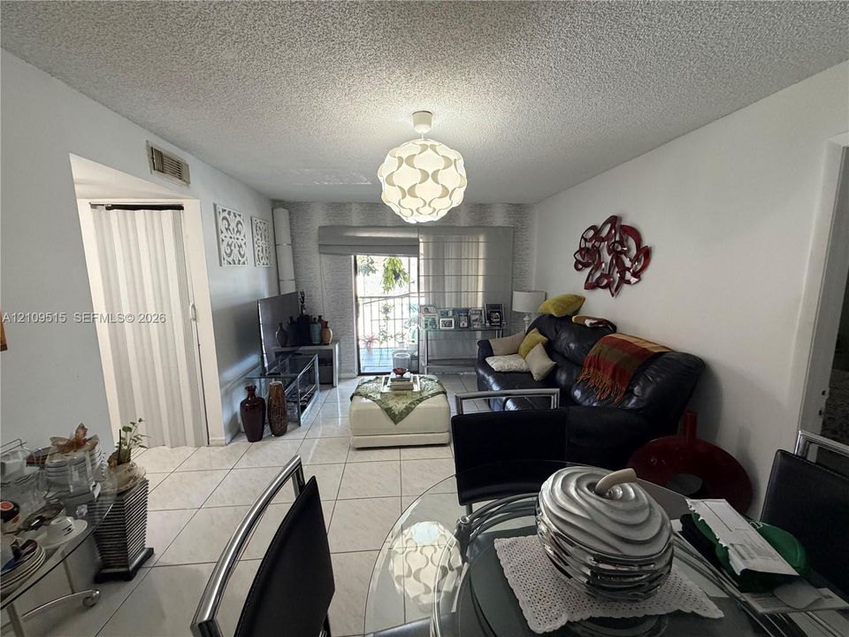Living area featuring large-format tile flooring, textured ceiling, pendant lighting, and a sliding glass door providing external access