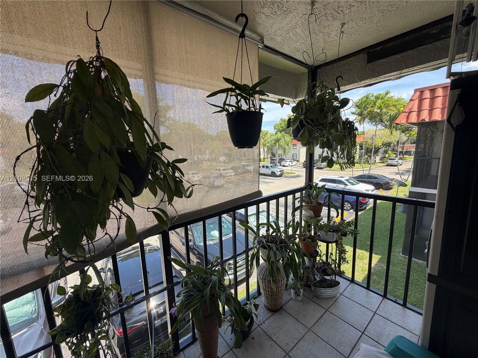 Screened-in balcony featuring tile flooring, metal railings, and a retractable privacy shade