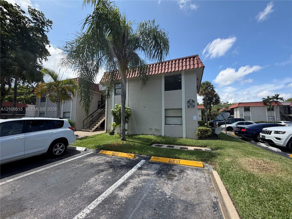 Stucco exterior featuring a clay tile roof, mature palm trees, and designated surface parking