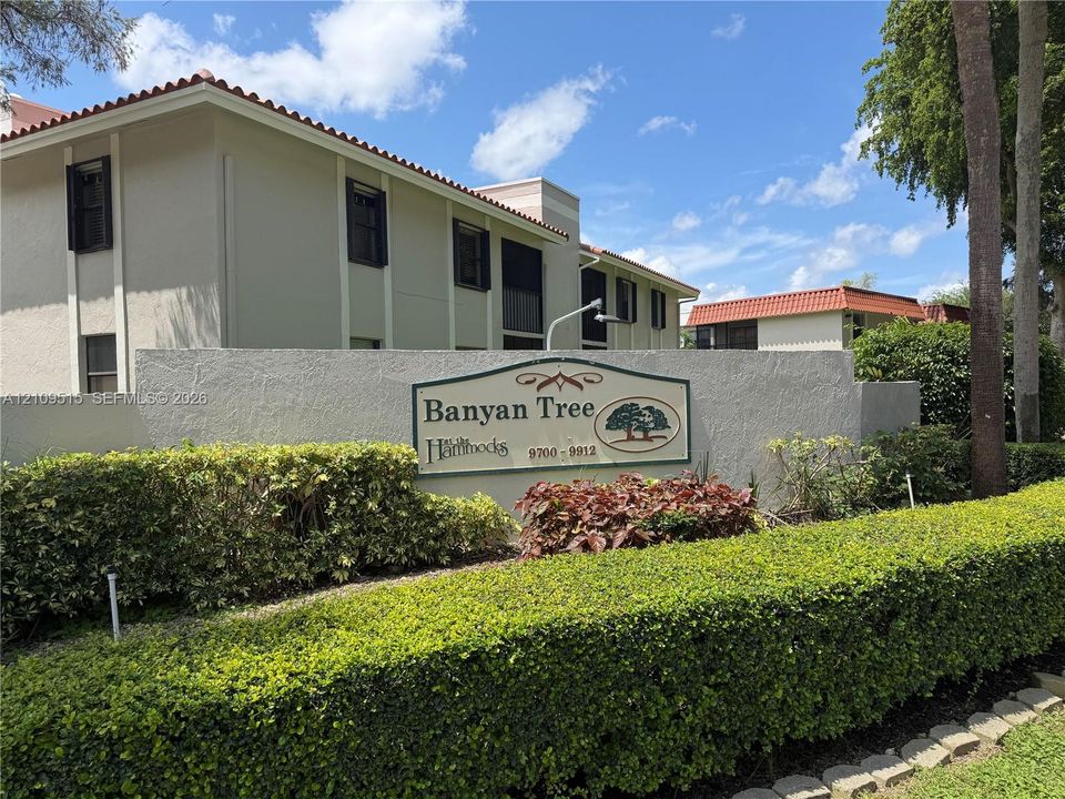 Multi-story building with textured stucco exterior, terra cotta-style roofing, and mature perimeter landscaping