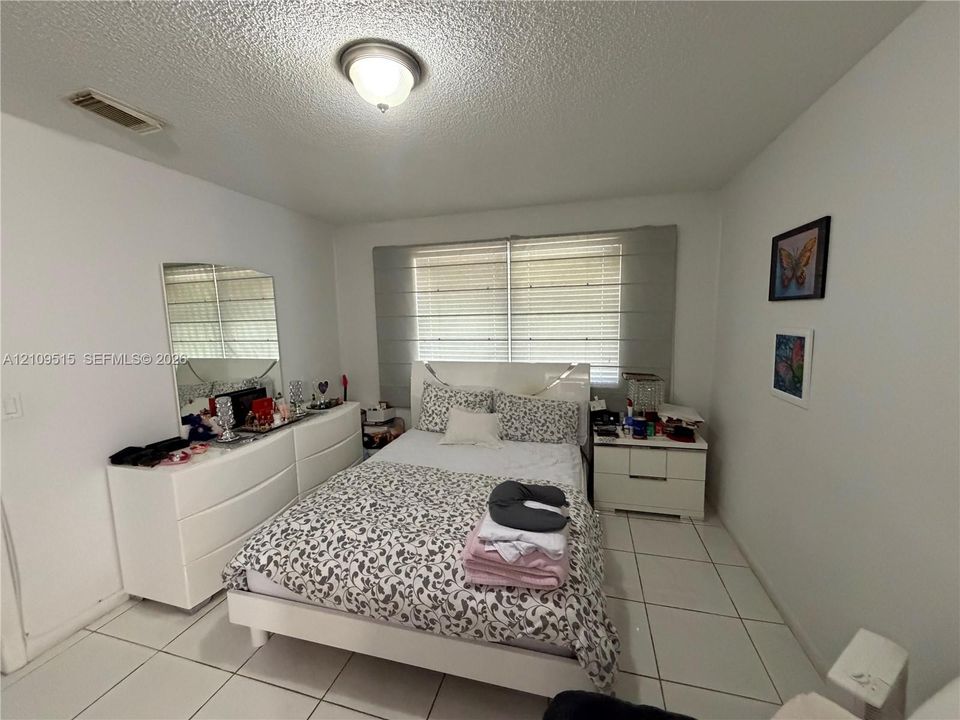 Room featuring white tile flooring, neutral walls, and a ceiling-mounted light fixture, complemented by horizontal window blinds