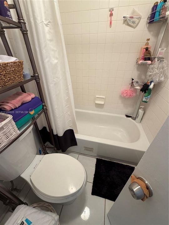 Bathroom featuring a white porcelain commode, a built-in bathtub, and ceramic wall tile surround