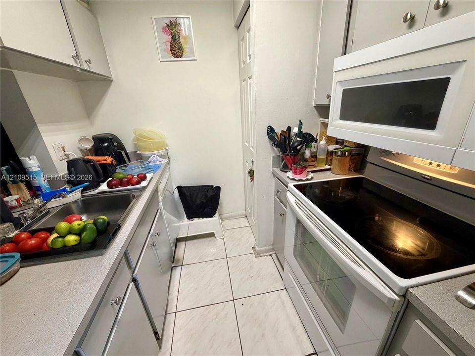 Kitchen featuring white cabinetry, solid surface countertops, stainless steel sink, built-in microwave, and tile flooring
