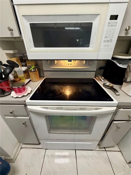 White electric range with a smooth-top surface, integrated over-the-range microwave, solid-surface countertops, and light-toned cabinet hardware
