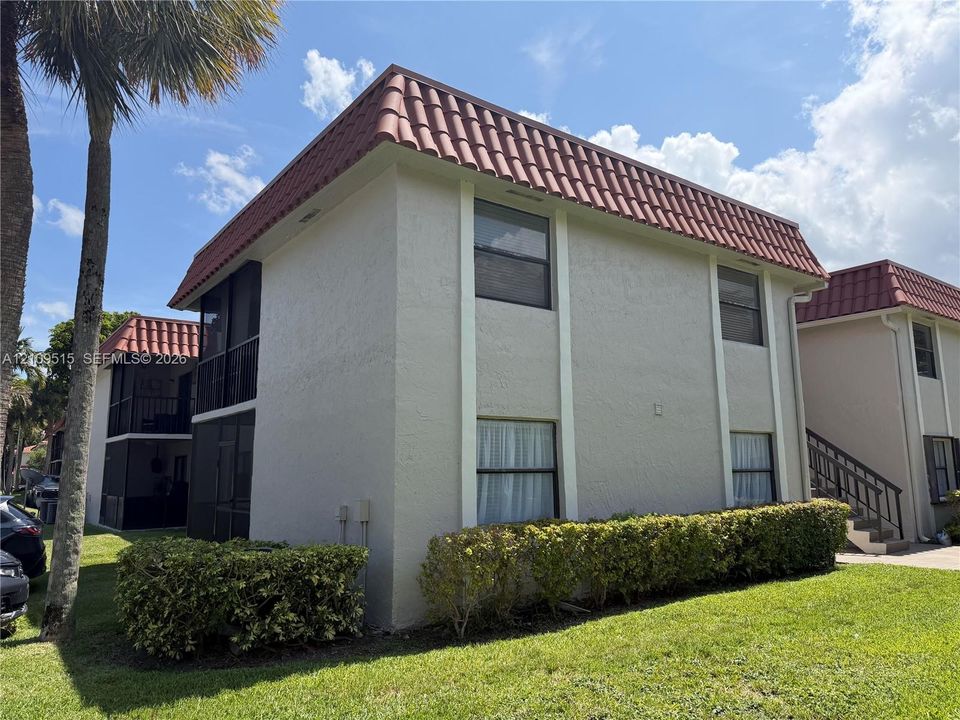Two-story exterior featuring light-colored stucco siding, a red tile mansard roof, screened-in balconies, and manicured shrubbery