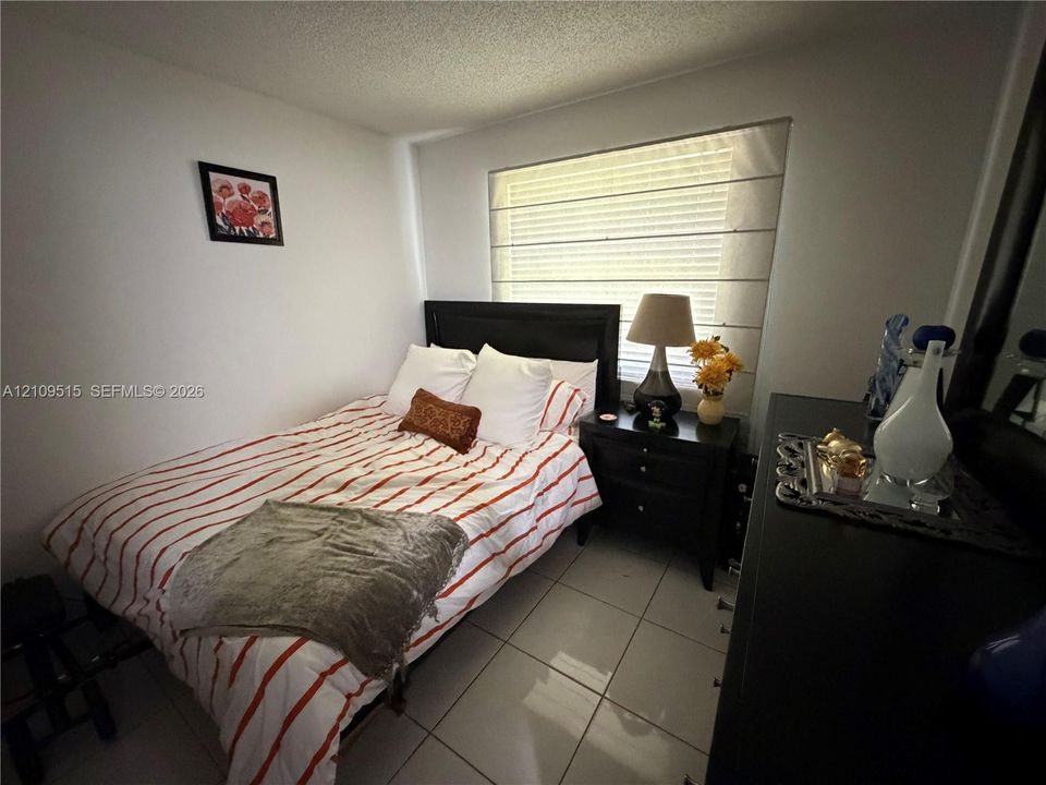 Neutral-toned room featuring large-format tile flooring, textured ceilings, and a window with integrated shade treatment