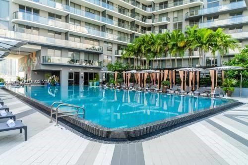 Swimming pool with tile surround, multi-story structure with glass-panel balconies, concrete patio decking, and established palm trees