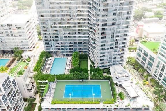 High-rise residential building featuring a blue-surfaced tennis court, swimming pool, landscaped lawn, and multiple levels of private balconies