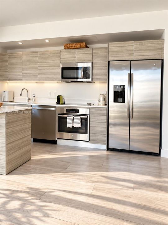 Kitchen featuring horizontal-grain wood-finish cabinetry, stainless steel appliances, solid-surface countertops, recessed ceiling lighting, and wood-finish flooring