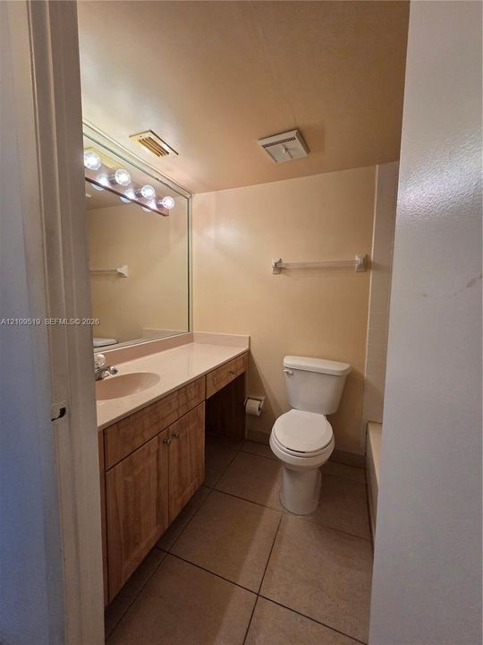 Bathroom featuring a vanity with wood-finish cabinetry, a solid-surface countertop, an integrated sink, a full-width wall mirror, and tiled flooring