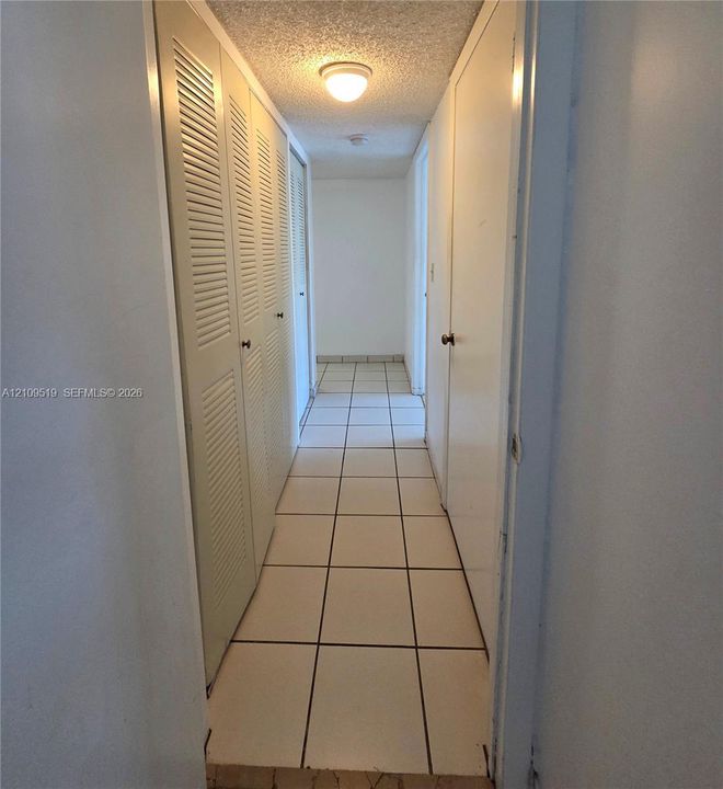 Room featuring large-format tile flooring, two closets with louvered bi-fold doors, and a solid-core interior door