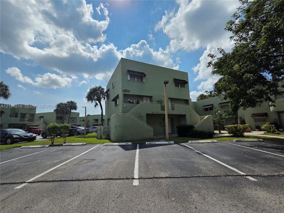Multi-level building exterior featuring smooth stucco siding, fixed window awnings, and an outdoor staircase with concrete railings