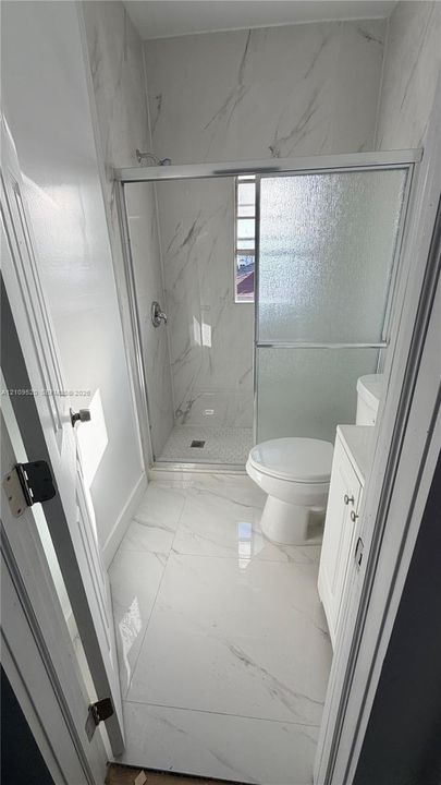 Bathroom featuring large-format veined tile flooring, full-height tile shower surround, sliding glass shower door, and white cabinetry