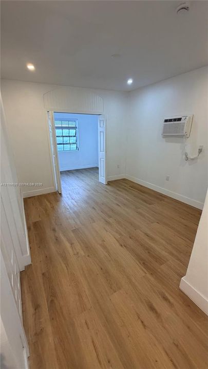 Wood-finish flooring, recessed lighting, wall-mounted air conditioning unit, and double-panel entry door