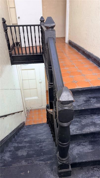 Staircase featuring dark-finished wooden treads and ornate turned balusters, accompanied by terracotta-style tile flooring and a minimalist wall-mounted handrail