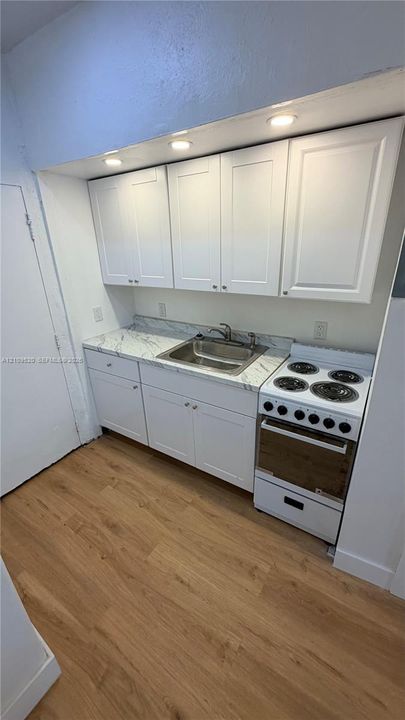 Kitchen area featuring white shaker-style cabinetry, stone-patterned countertops, a stainless steel drop-in sink, an integrated electric range, and wood-finish flooring