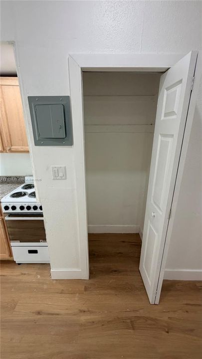 Closet with overhead shelf, wood-finish flooring, white paneled door, and proximity to electric service panel