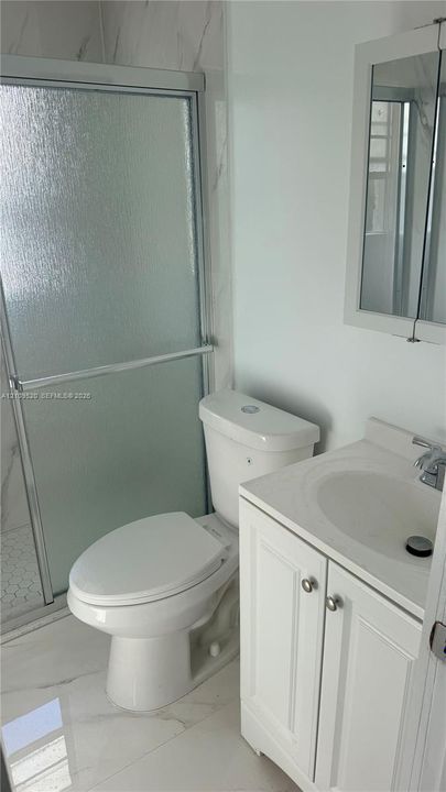 Bathroom featuring a shower with a sliding glass door, a vanity with a white countertop and basin, and a built-in mirrored medicine cabinet
