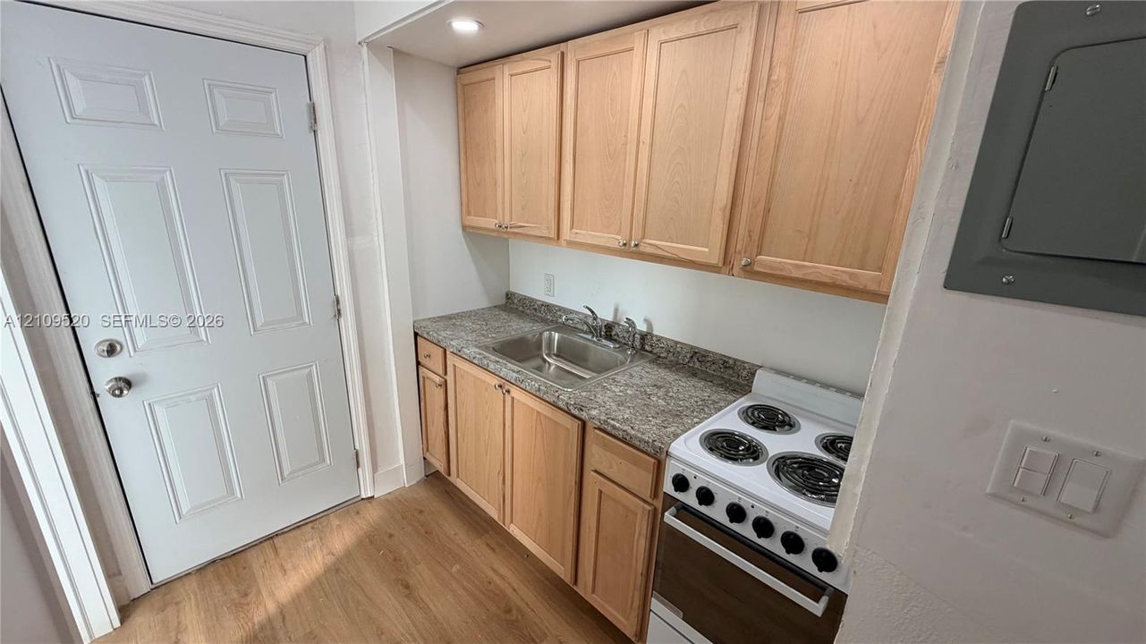 Kitchen featuring wood-finish cabinetry, stone-patterned countertops, integrated stainless steel sink, electric range, and wood-finish flooring