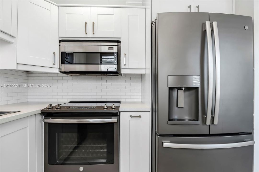 White shaker-style cabinetry, stainless steel microwave, matte-finish range, French-door refrigerator, and white subway tile backsplash