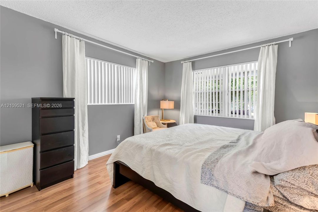 Wood-finish flooring, neutral wall paint, and dual windows featuring vertical blinds