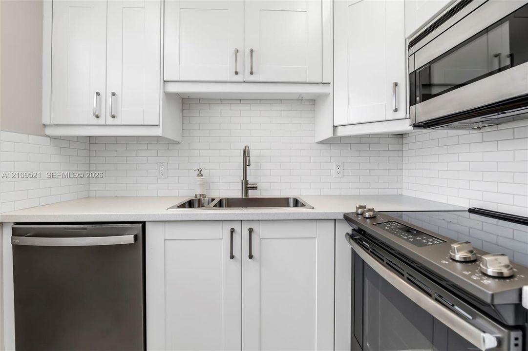 Kitchen featuring white shaker-style cabinetry, white subway tile backsplash, stainless steel appliances, and a dual-basin stainless steel sink