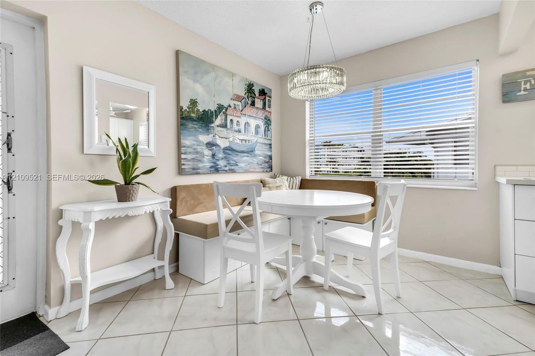 Dining area featuring neutral tile flooring, built-in corner bench seating, a circular pendant light fixture, and horizontal blind window treatments