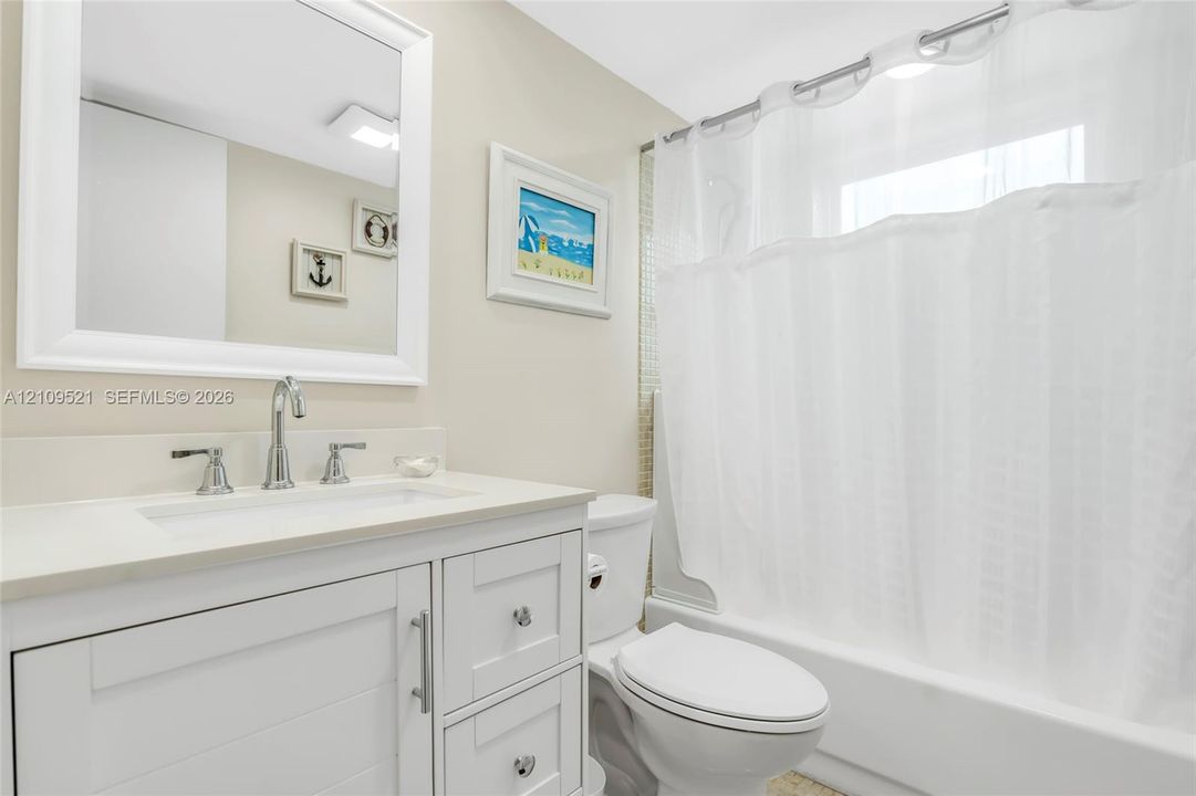 Bathroom featuring a white vanity cabinet, solid-surface countertop with an integrated sink, polished chrome faucet, framed wall mirror, and a tile-surround shower and tub combination