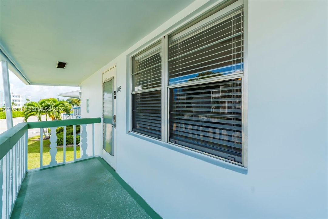 Covered exterior balcony featuring a solid-surface floor, painted railing with decorative posts, and horizontal sliding windows