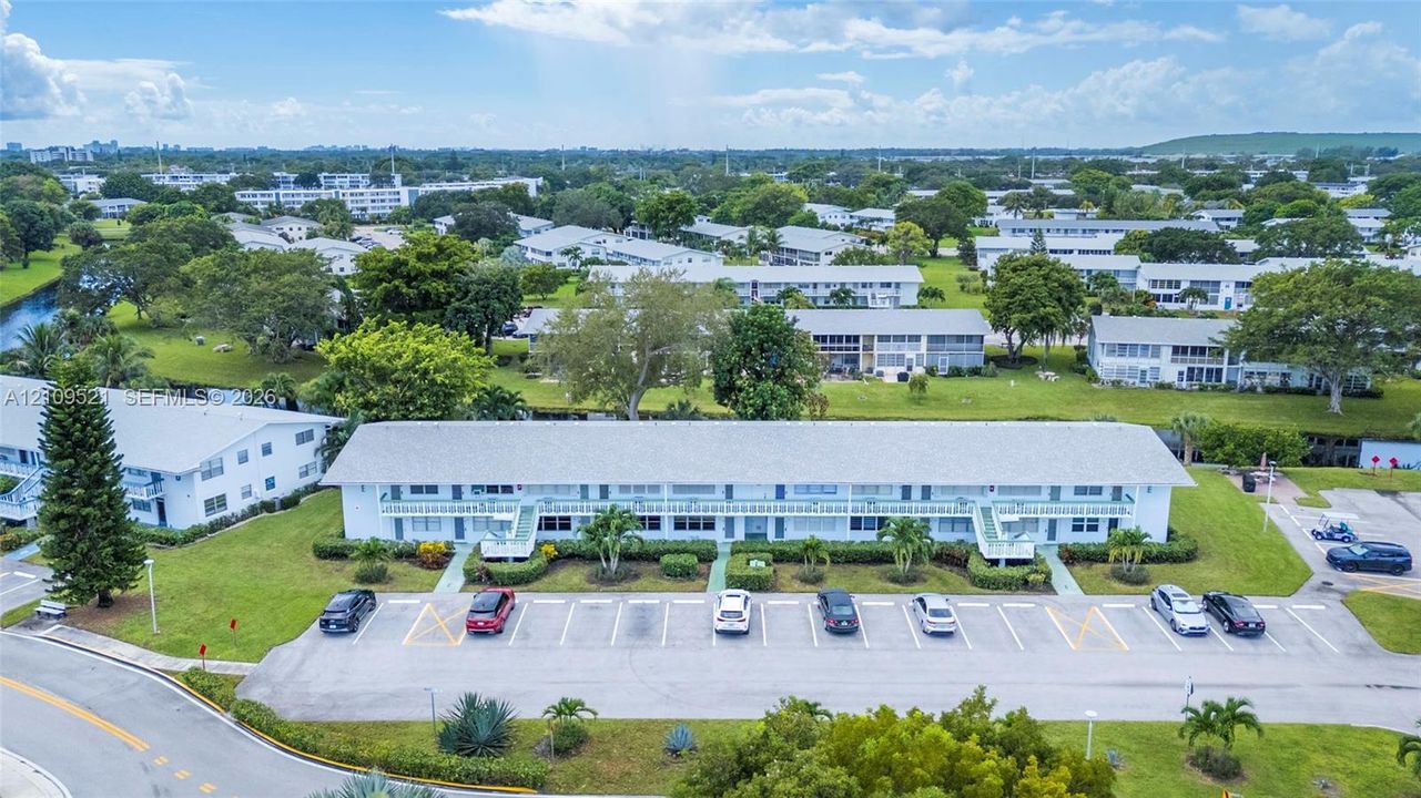 Aerial perspective of a multi-story residential building featuring exterior staircases, a dedicated surface parking lot, and mature landscaping