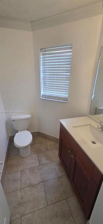 Bathroom featuring a vanity with wood-finish cabinetry, a white integrated countertop and sink, neutral tile flooring, and crown molding