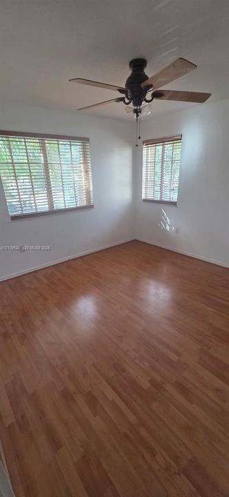 Room interior featuring wood-finish flooring, two windows with horizontal blinds, and a ceiling fan with integrated lighting