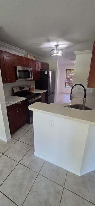 Kitchen featuring stained wood cabinetry, white countertops, tile flooring, stainless steel appliances, and a high-arc kitchen faucet