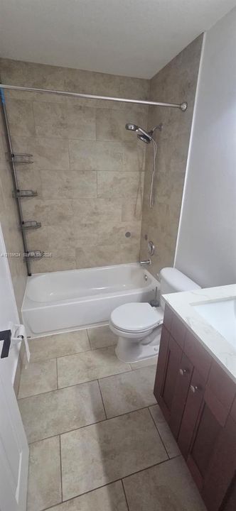 Bathroom featuring large-format tile flooring, a tub-shower combination with full-height wall tile surround, built-in metal shelving, a vanity with a stone-composite countertop, and an integrated basin