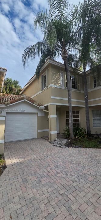 Two-story exterior featuring a stucco facade, tiled roof, attached single-car garage, and paver driveway