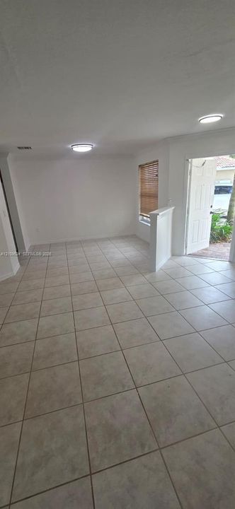 Neutral-toned tile flooring, recessed ceiling lighting, and a half-height partition wall with a single-pane window featuring horizontal blinds