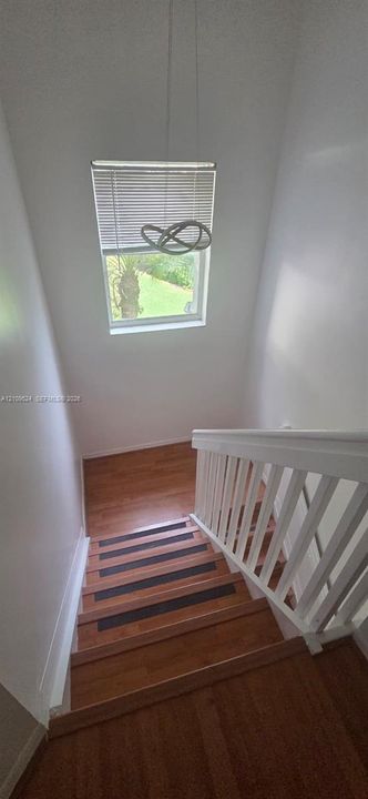 Staircase featuring wood-finish treads with central anti-slip inlays, white wooden balustrade, single-hung window with internal blinds, and a suspended contemporary light fixture