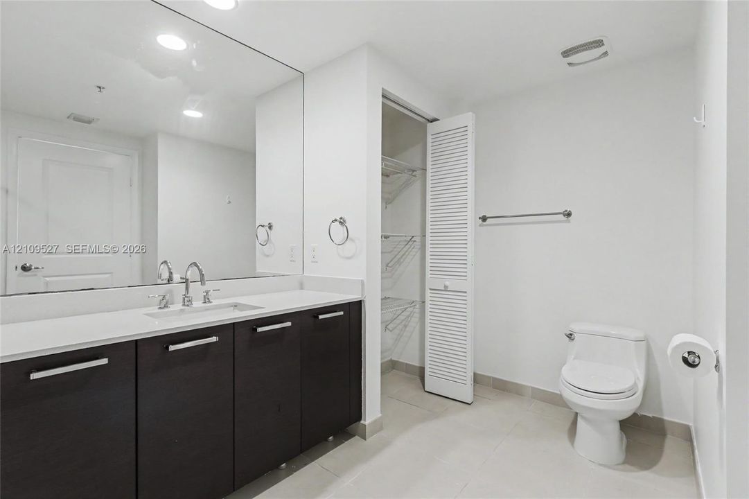 Bathroom featuring a dark wood-finish vanity with a light-toned countertop, undermount sink, expansive wall-mounted mirror, louvered-door closet, and tile flooring