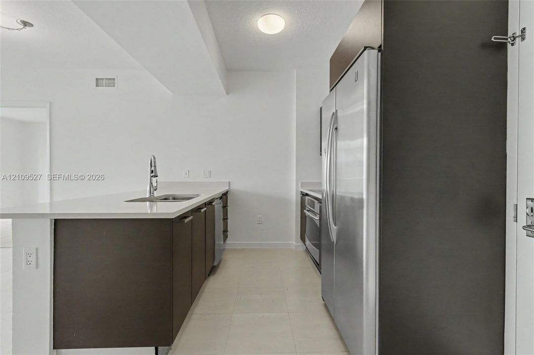 Kitchen featuring a solid-surface countertop, stainless steel refrigerator, undermount sink with a pull-down faucet, and dark wood-finish cabinetry