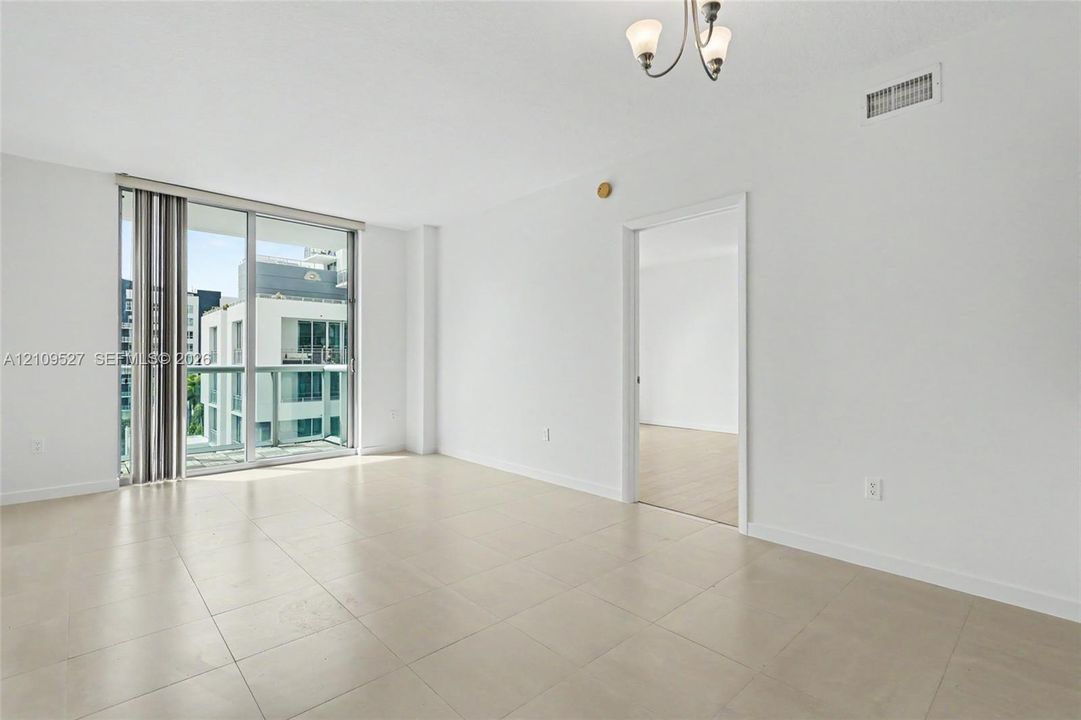 Open-concept room featuring oversized floor-to-ceiling sliding glass doors, neutral tile flooring, and a three-arm chandelier