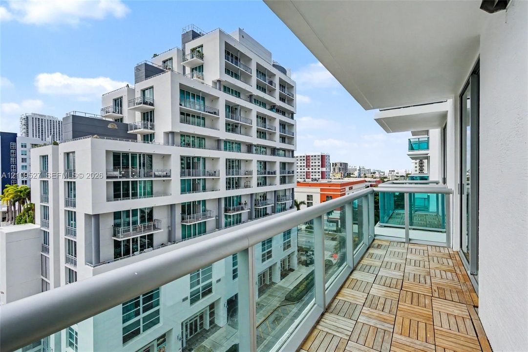 Private balcony featuring modular wood-finish decking and a glass-panel railing