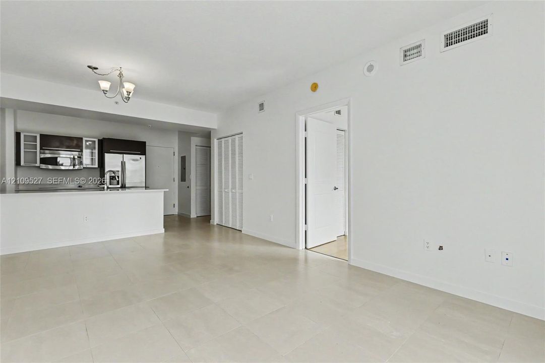 Open-concept interior featuring neutral tile flooring, kitchen with dark cabinetry, stainless steel appliances, breakfast bar, and multi-light ceiling fixture