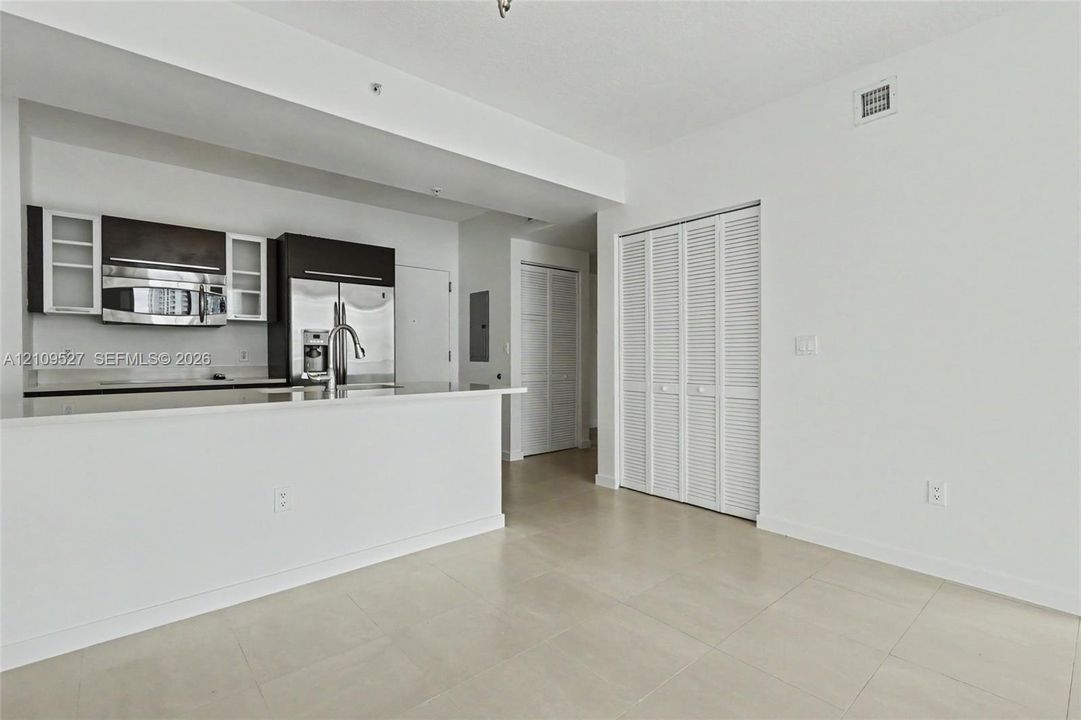 Kitchen featuring dark wood-finish cabinetry, stainless steel appliances, stone-surfaced breakfast bar, and large-format tile flooring with louvered closet doors