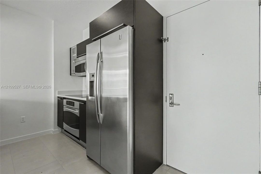 Kitchen featuring dark flat-panel cabinetry, stainless steel side-by-side refrigerator, built-in microwave, integrated oven, and light-toned tile flooring