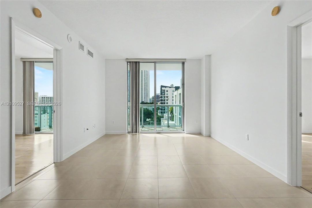 Open-concept interior featuring large-format tile flooring, floor-to-ceiling glass sliding doors, and a glass-paneled balcony