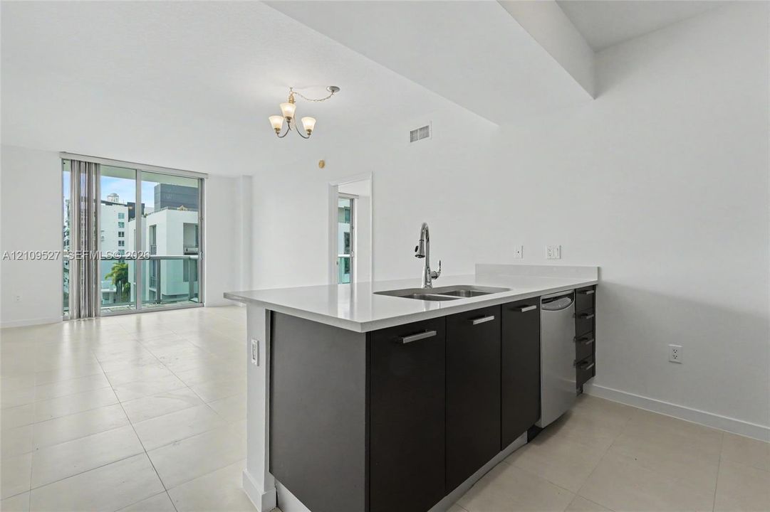 Kitchen featuring dark-finish cabinetry, quartz countertops, a dual-basin stainless steel sink with a high-arch faucet, tile flooring, and floor-to-ceiling glass sliding doors