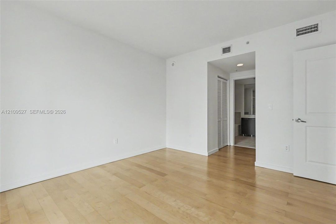 Room featuring wood-finish flooring, white walls, paneled interior door, and louvered-style closet door