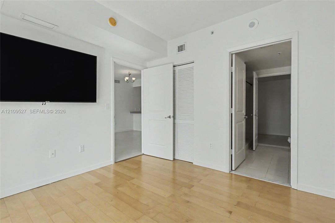 Room with wood-finish flooring, white walls, louvered closet doors, and panel-style interior doors