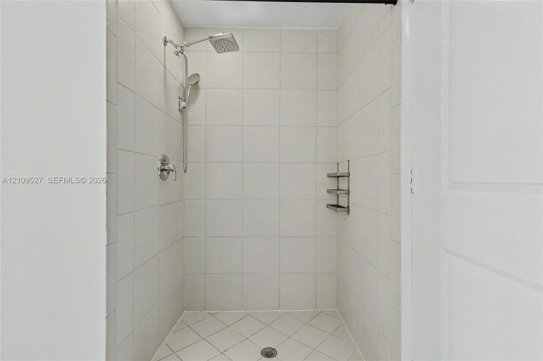 Walk-in shower featuring white wall tiling, diamond-patterned floor tile, a rainfall showerhead, a handheld sprayer attachment, and a built-in recessed shelf