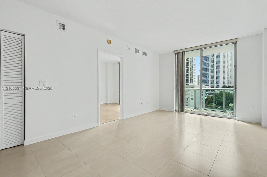 Neutral-toned tile flooring, louvered closet doors, and floor-to-ceiling glass sliding doors opening to a balcony